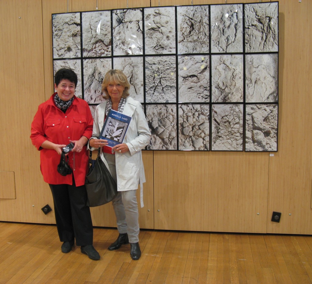 Mireille Dabée (à gauche), devant l'ensemble intitulé "Pierres de Palmyre" composé de 21 tableaux, fait de sept triptyques verticaux accolés sur trois strates.